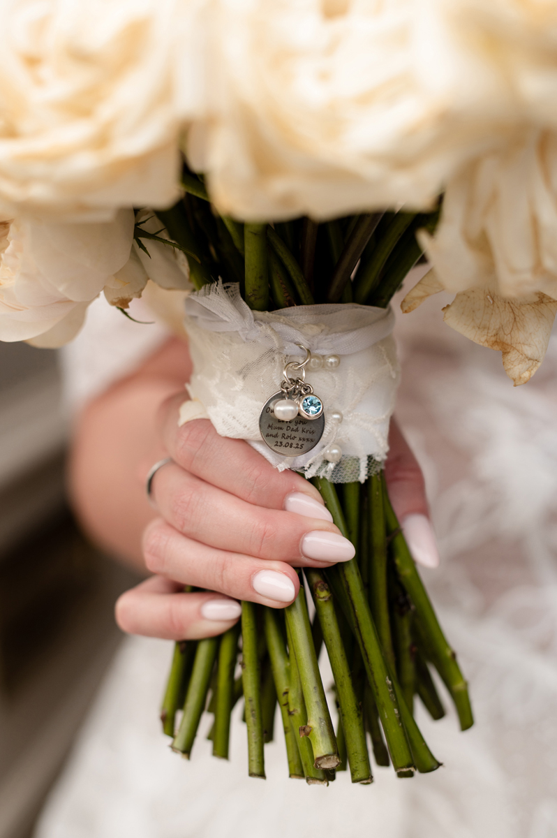 Close-up of white rose bridal bouquet with personalised memorial charm at a Crossbasket Castle wedding near Glasgow.