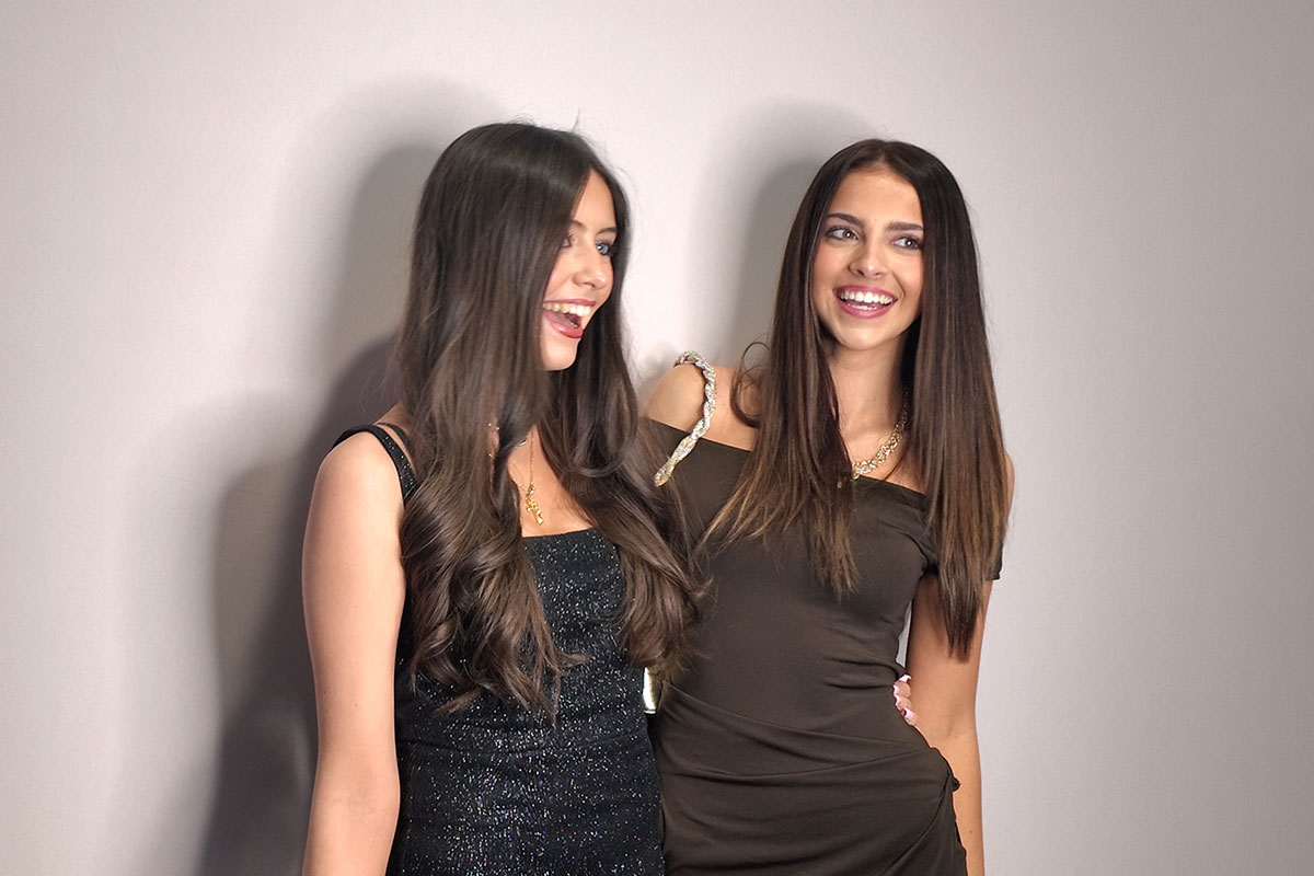 Two women posing at event photo booth wearing evening dresses, smiling for professional photo booth portrait