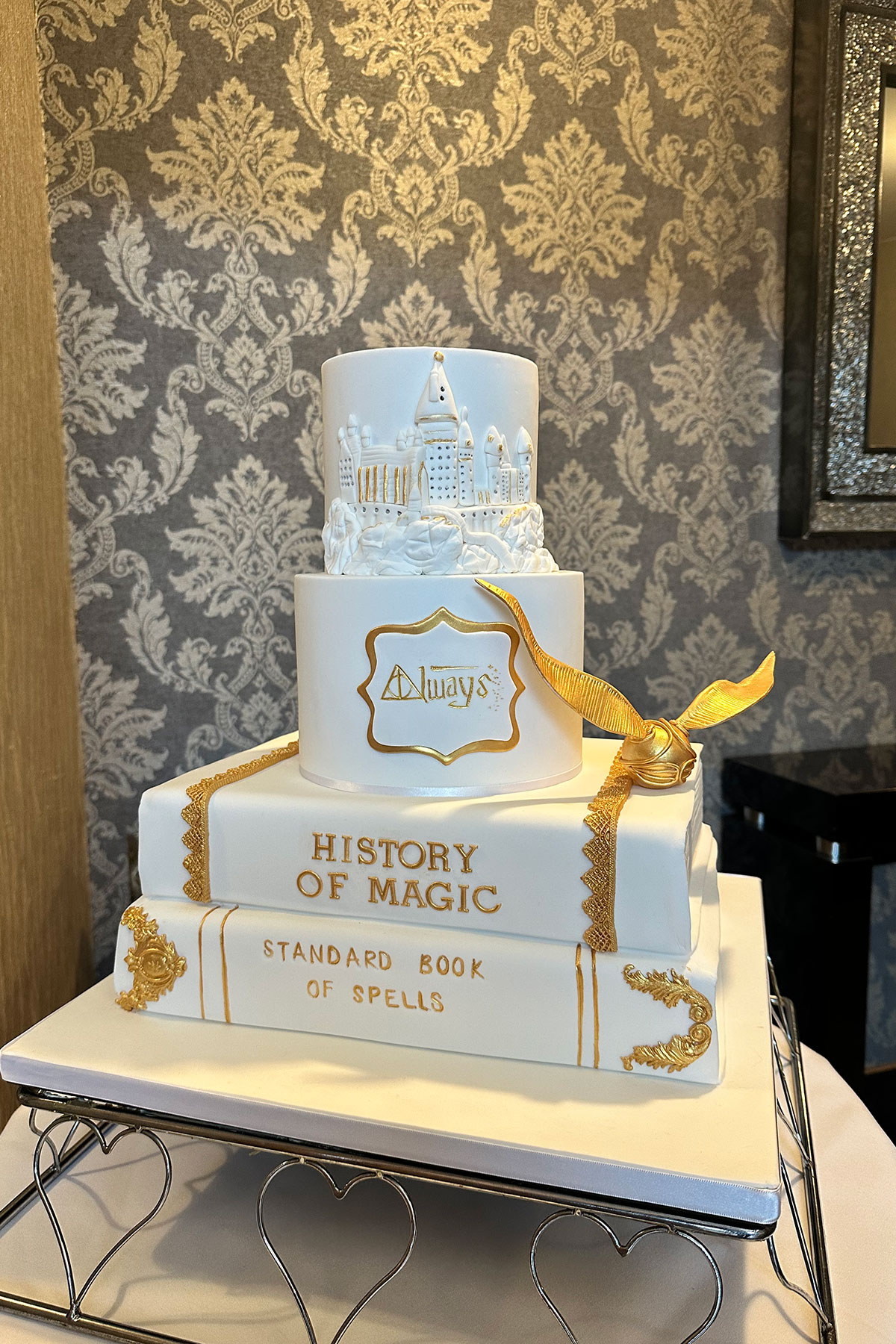 four tier white fondant cake with Harry Potter theme – the two bottom tiers are book shaped, while the top two are round, and gold detailing decorates the cake