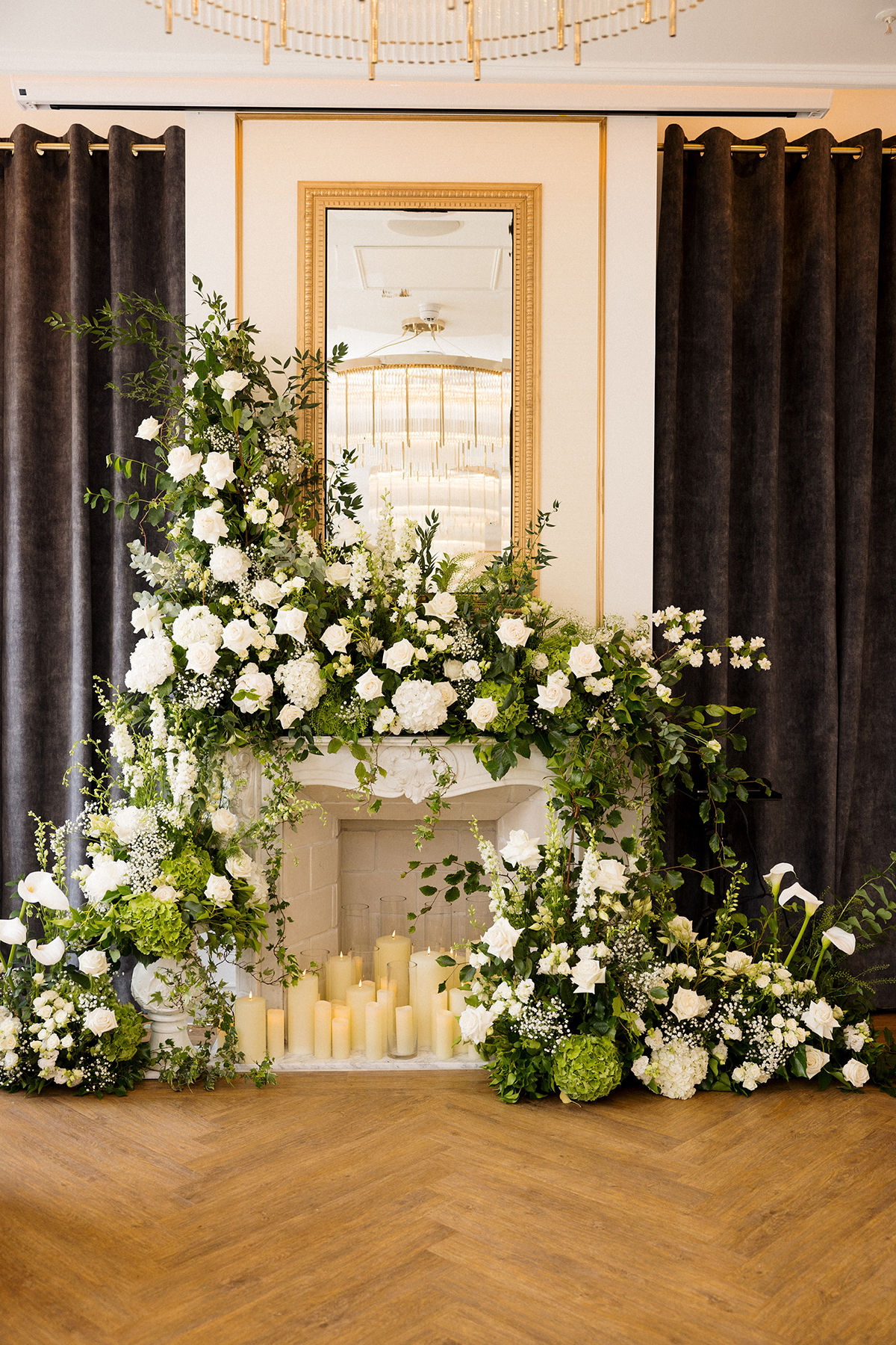 White and green wedding flowers and candles arranged around a fireplace ceremony backdrop