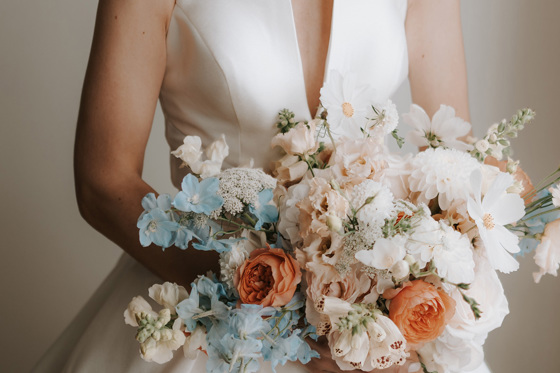 Bride holding blue, orange, pink and white bouquet