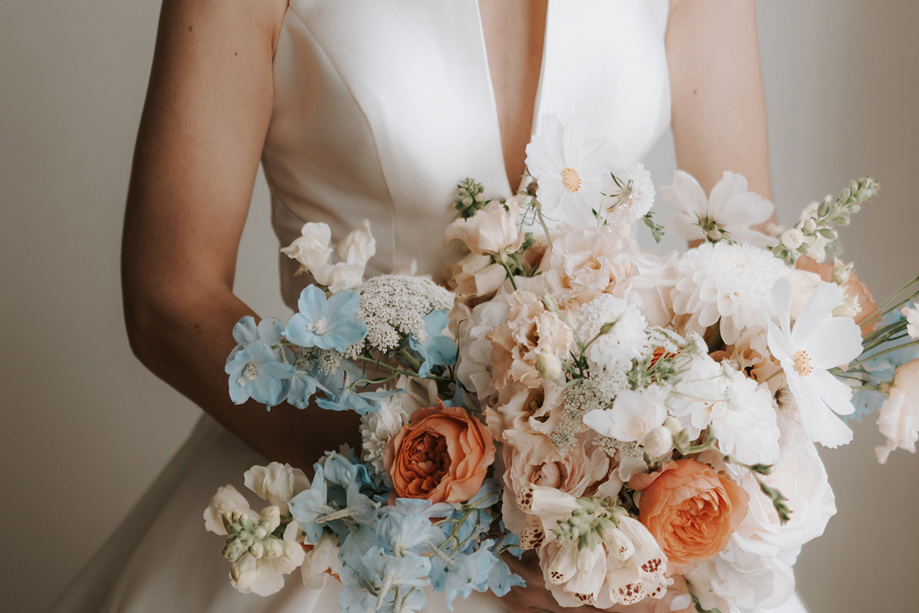 Bride holding blue, orange, pink and white bouquet
