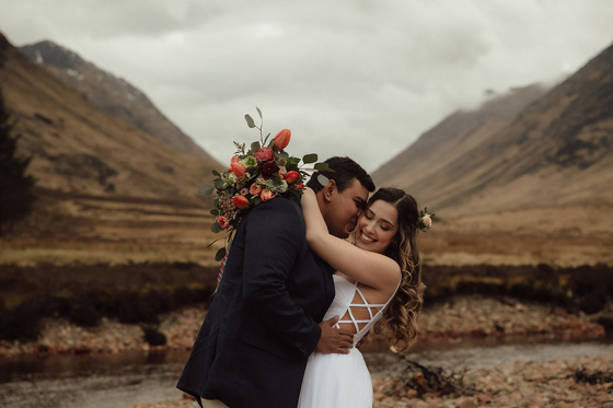 Groom kissing brides cheek standing amongst hills with tulip bouquet