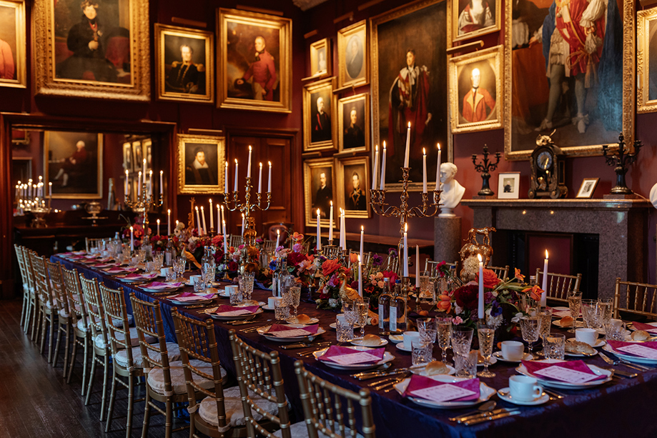 Long banquet wedding table styled with candles and florals inside a historic dining room with framed portraits