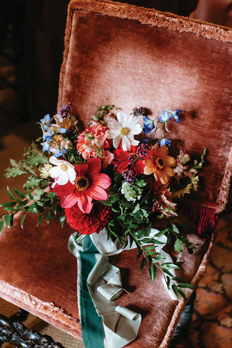 Colourful wildflower bridal bouquet styled on a rust velvet chair for a relaxed, modern wedding
