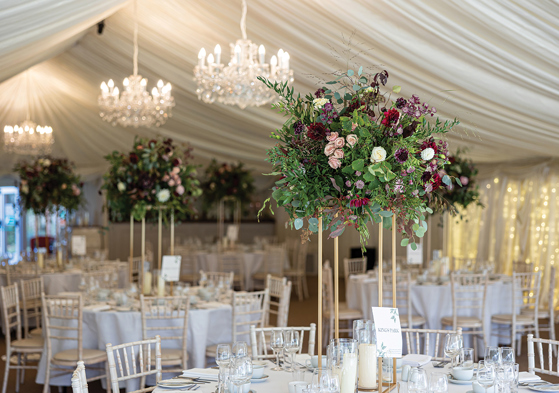 Statement floral centrepiece on gold stand styled on wedding reception tables inside a marquee