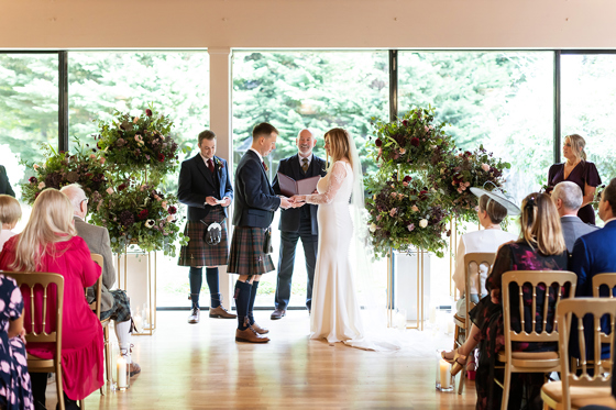 Wedding ceremony with floral installations in cream, blush and red on stands framing the couple