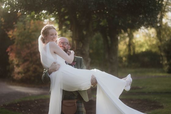 Bride laughing as groom carries her across the grass at a Scottish wedding planned by Pebblefish Occasions & Events.