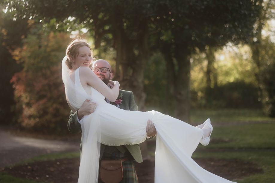 Bride laughing as groom carries her across the grass at a Scottish wedding planned by Pebblefish Occasions & Events.