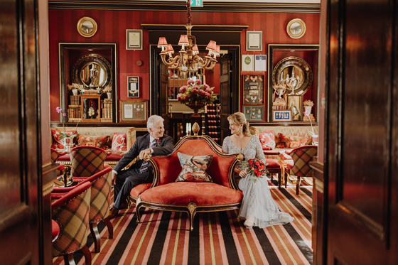 Newlywed couple seated in a richly decorated red lounge at a Scottish wedding planned by Pebblefish Occasions & Events.