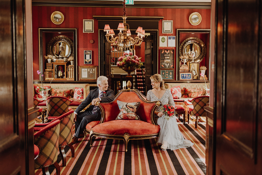 Newlywed couple seated in a richly decorated red lounge at a Scottish wedding planned by Pebblefish Occasions & Events.