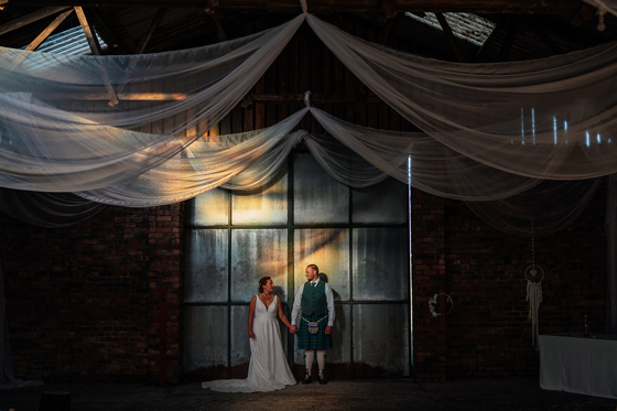 Bride and groom holding hands beneath draped fabric in an industrial wedding venue planned by Pebblefish Occasions & Events.