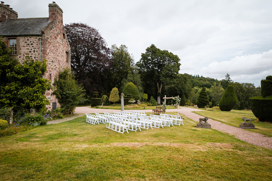 Outdoor wedding ceremony setup with white chairs and floral arch in historic Scottish gardens, planned by Pebblefish Occasions & Events.