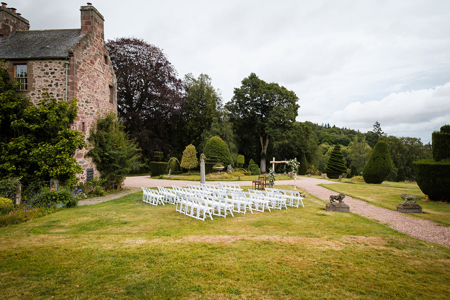Outdoor wedding ceremony setup with white chairs and floral arch in historic Scottish gardens, planned by Pebblefish Occasions & Events.