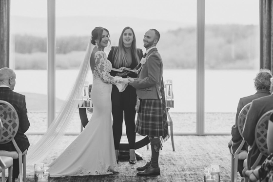 Black and white image of smiling couple holding hands at altar with celebrant