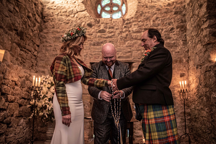 Celebrant tying the knot for couple in tartan at altar with candles in background