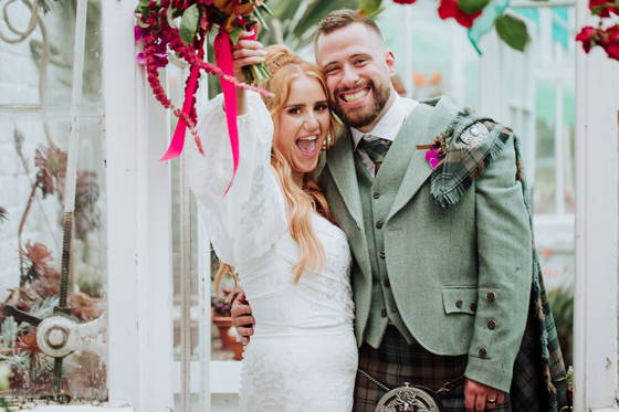 Happy newlyweds posing after their wedding ceremony, with the bride holding a pink bouquet and the groom smiling beside her.