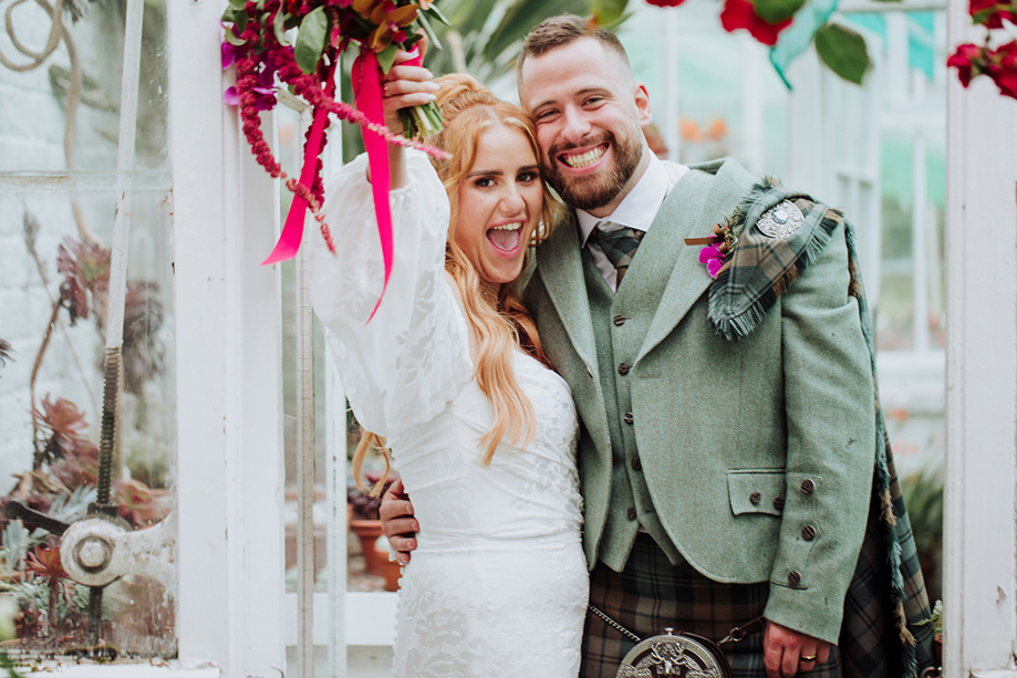 Happy newlyweds posing after their wedding ceremony, with the bride holding a pink bouquet and the groom smiling beside her.
