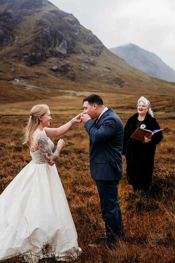 Intimate Glencoe elopement ceremony in the Scottish Highlands, with a humanist celebrant officiating as the groom kisses the bride’s hand during their outdoor wedding.