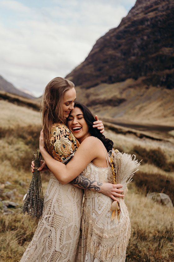 Close-up of brides laughing and hugging, holding dried flower bouquets during boho wedding shoot in Glencoe