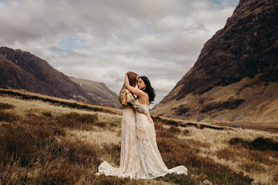 Intimate moment between brides in lace wedding dresses in Glencoe valley, surrounded by Highland mountains
