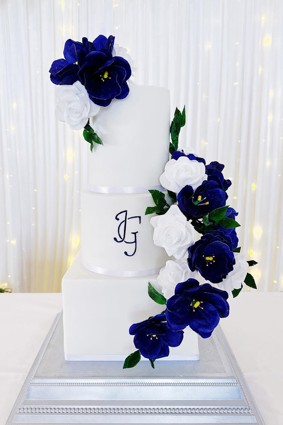 Three-tier blue and white cake with blue flowers and initials