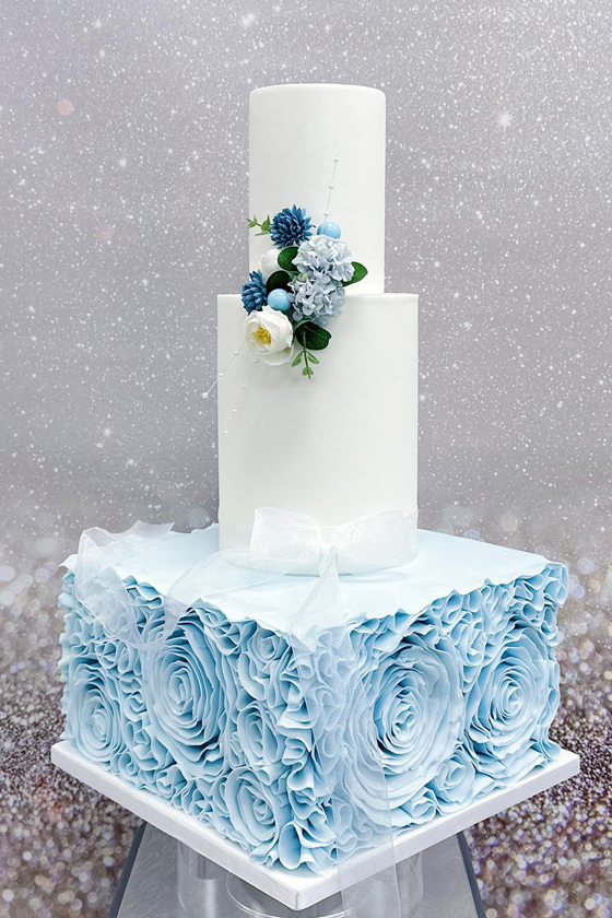 Three tier blue and white cake with large, blue square bottom tier with flowers