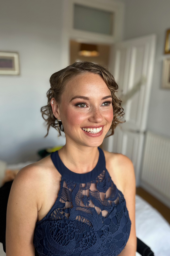 Bridesmaid in navy dress smiles with sun-kissed skin and matching blush and lipstick