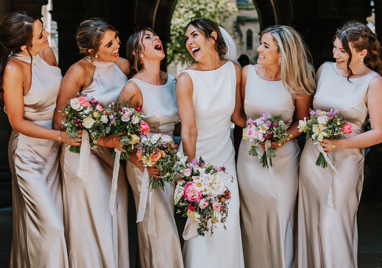 Bride and her bridesmaids laughing with bouquets in hand