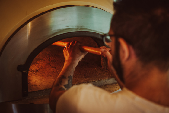 Owner of Dough Man's Land taking pizza out of oven