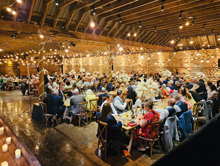 Busy barn wedding reception with guests dining under warm fairy lights