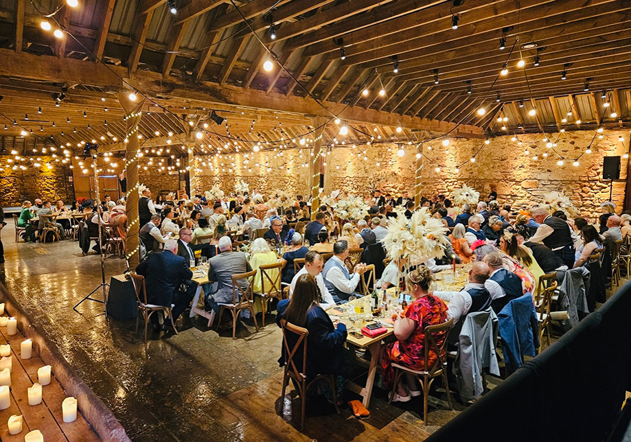 Busy barn wedding reception with guests dining under warm fairy lights