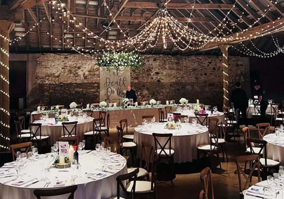Rustic barn wedding reception with fairy lights, round tables and evening atmosphere
