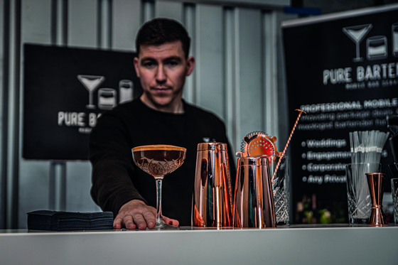 Owner of Pure Bartending Michael Mckenzie behind the bar pushing cocktail to front