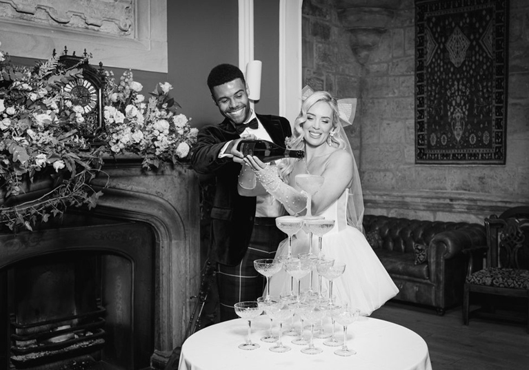 Black and white image of a bride and groom pouring champagne on a tower of glasses