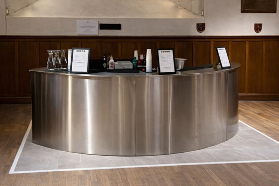 Curved stainless steel mobile bar by Sips Events positioned inside a historic event venue for drinks service.