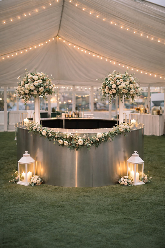 Circular wedding bar by Sips Events decorated with flowers, candles and lanterns inside a marquee reception.