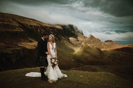 Bride and groom pose on top of a cloudy hill in the Scottish Highlands.