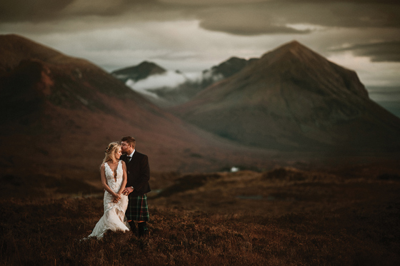 Bride and groom pose amongst Scottish Highlands hills.