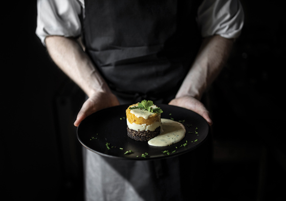 The Lunchbox Boys employee holds a black plate with haggis, neeps and tatties with tartar sauce.