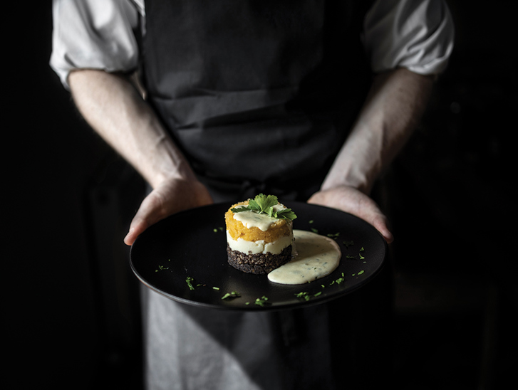 The Lunchbox Boys employee holds a black plate with haggis, neeps and tatties with tartar sauce.