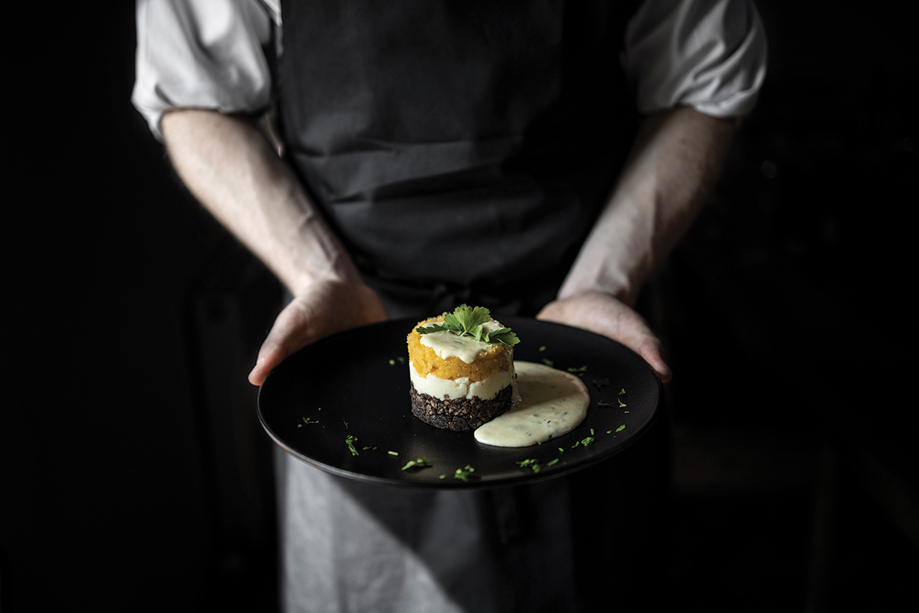 The Lunchbox Boys employee holds a black plate with haggis, neeps and tatties with tartar sauce.