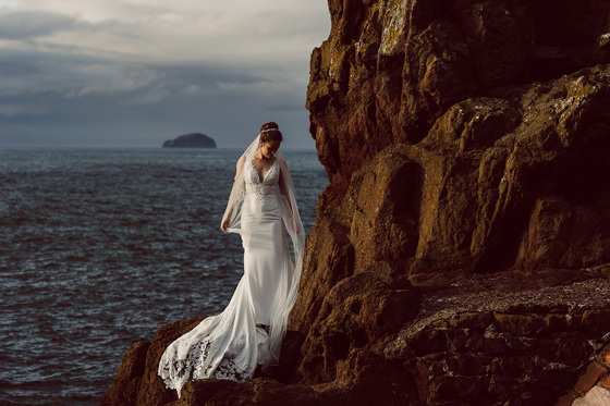 Bride stands on rocks at the sea