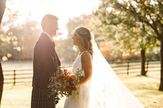 Bride and groom look at each other smiling with sun shining behind them