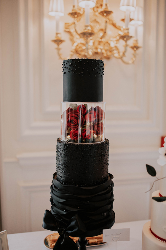 Four-tier, black cake with acrylic, rose-filled tier and pearl, sparkle and ribbon-like decorative icing