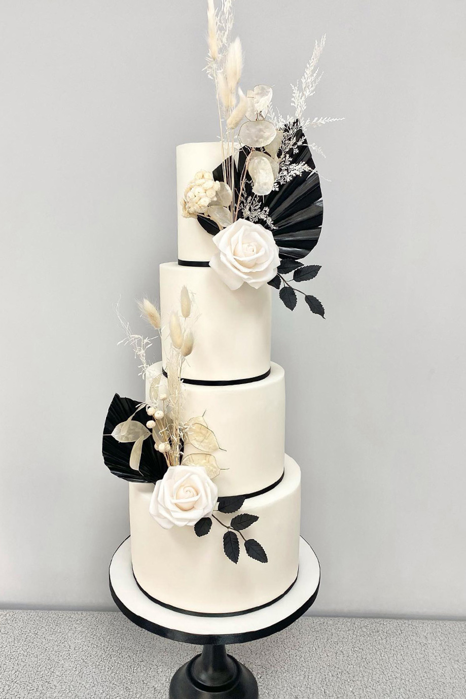 Monochrome four-tier cake with large black leaves, white roses and pampas grass