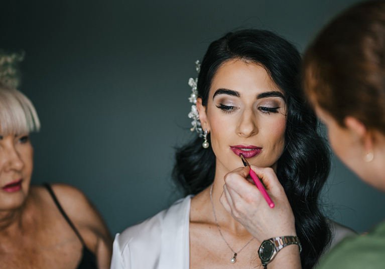 Nicola paints dark pink lipstick on a bride