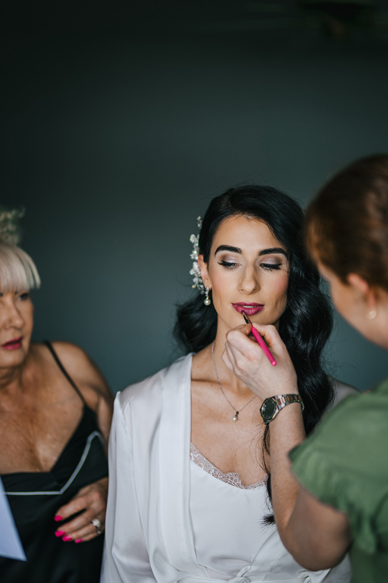 Nicola paints dark pink lipstick on a bride