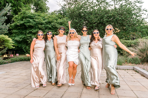 Bride and bridesmaids wearing heart-shaped sunglasses during a relaxed wedding portrait