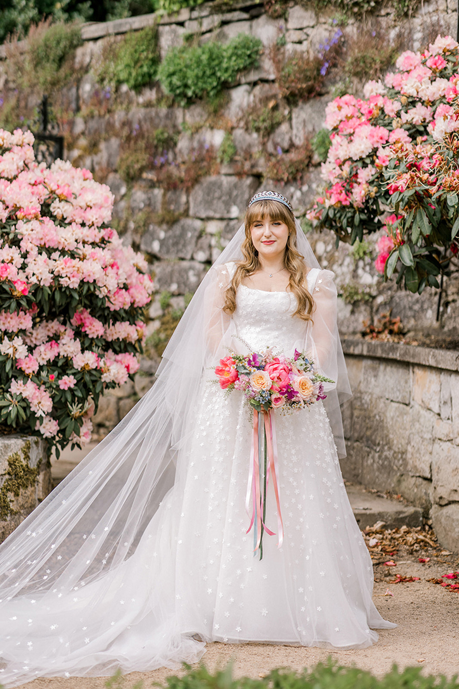 Bride holding a colourful bouquet in a Scottish wedding garden with pink flowers, photographed by The Gibsons